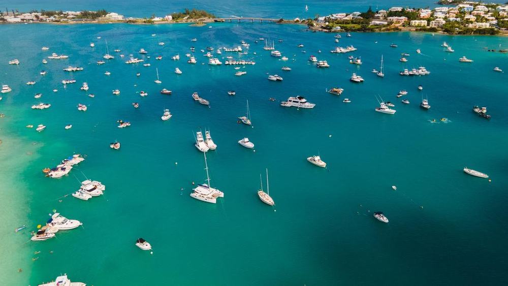 Aerial view of boats anchored in turquoise water near a small island with pastel houses