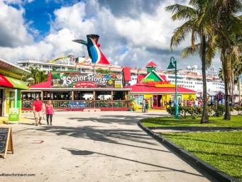Colourful waterfront restaurant and shops under palm trees with a cruise ship behind