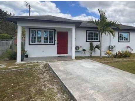 Front of the 3 bed, 2 bath home in Millennium Gardens, with a red door, carport and palm tree