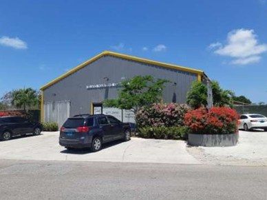 Front of the warehouse at Oakes Field, with a grey roof trimmed in yellow and flowering shrubs