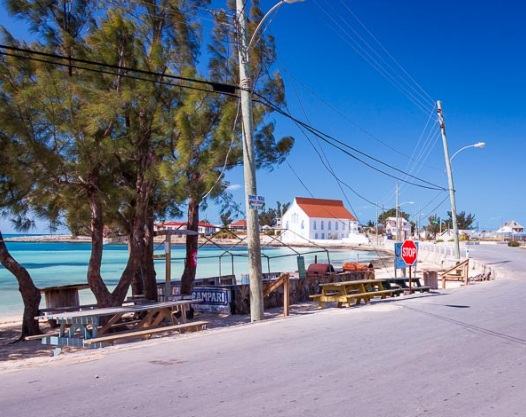 Quiet waterfront road in Eleuthera with picnic benches and a white building with a red roof