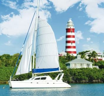 Red and white striped lighthouse behind a white catamaran in the Abacos